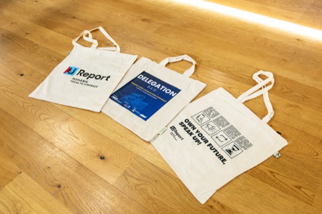 Three branded delegation tote bags laid out on a wooden floor.